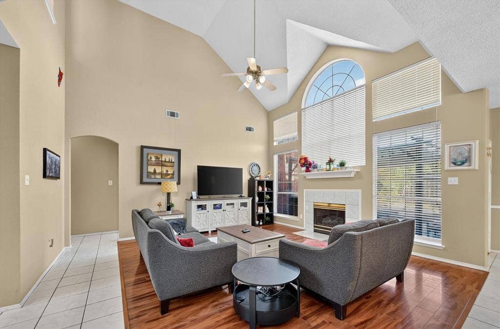 1625 Falmouth Drive, Plano, TX 75025 Vaulted ceiling living area featuring a fireplace with a tile surround, large windows, wood-finish flooring, and a ceiling fan