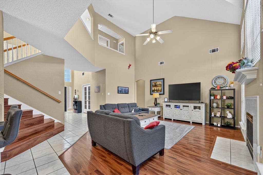 1625 Falmouth Drive, Plano, TX 75025 Two-story living area featuring vaulted ceilings, wood-finish flooring, a fireplace with a tile hearth, and a staircase with a wood handrail