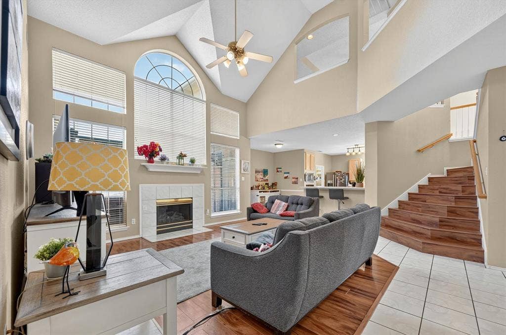 1625 Falmouth Drive, Plano, TX 75025 Two-story living area featuring a vaulted ceiling with a ceiling fan, a fireplace with a white tile surround and mantel, and large windows with an arched top window