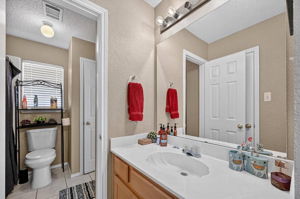 1625 Falmouth Drive, Plano, TX 75025 Full vanity mirror with sconce lighting, single basin sink, and wood-finish cabinetry