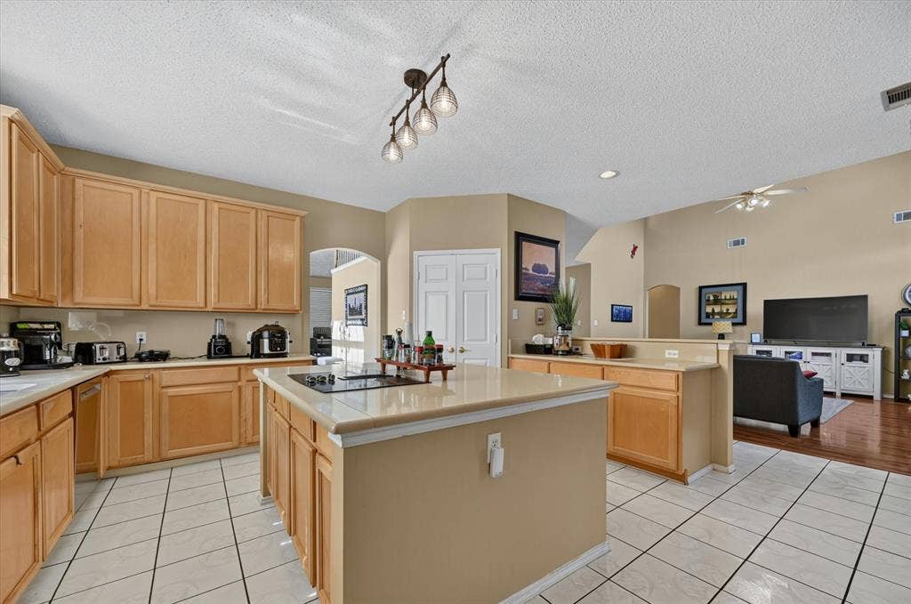 1625 Falmouth Drive, Plano, TX 75025 Spacious kitchen featuring light wood cabinetry, light-toned countertops, a central island with a cooktop, and tile flooring