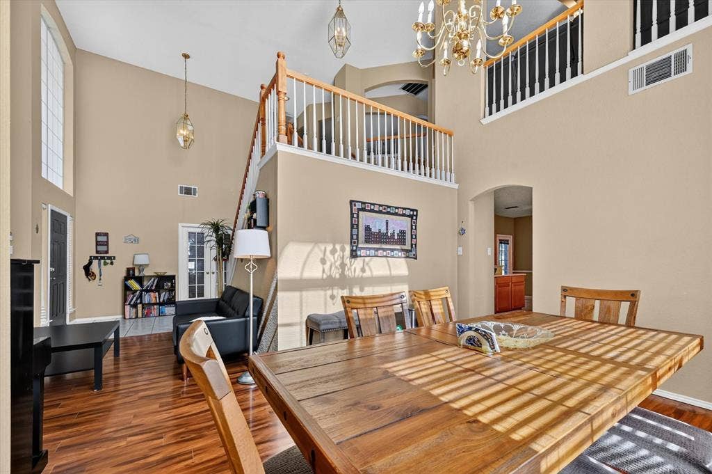 1625 Falmouth Drive, Plano, TX 75025 Spacious living area featuring double-height ceilings, wood-finish flooring, an upper-level balcony, and a prominent dining area with a chandelier