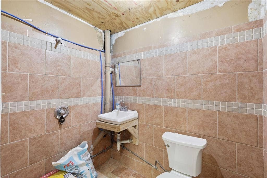 2136 California Crossing Road, Dallas, TX 75220 Bathroom featuring tan wall tiles with decorative mosaic accent bands, a wall-mounted sink, and a white toilet
