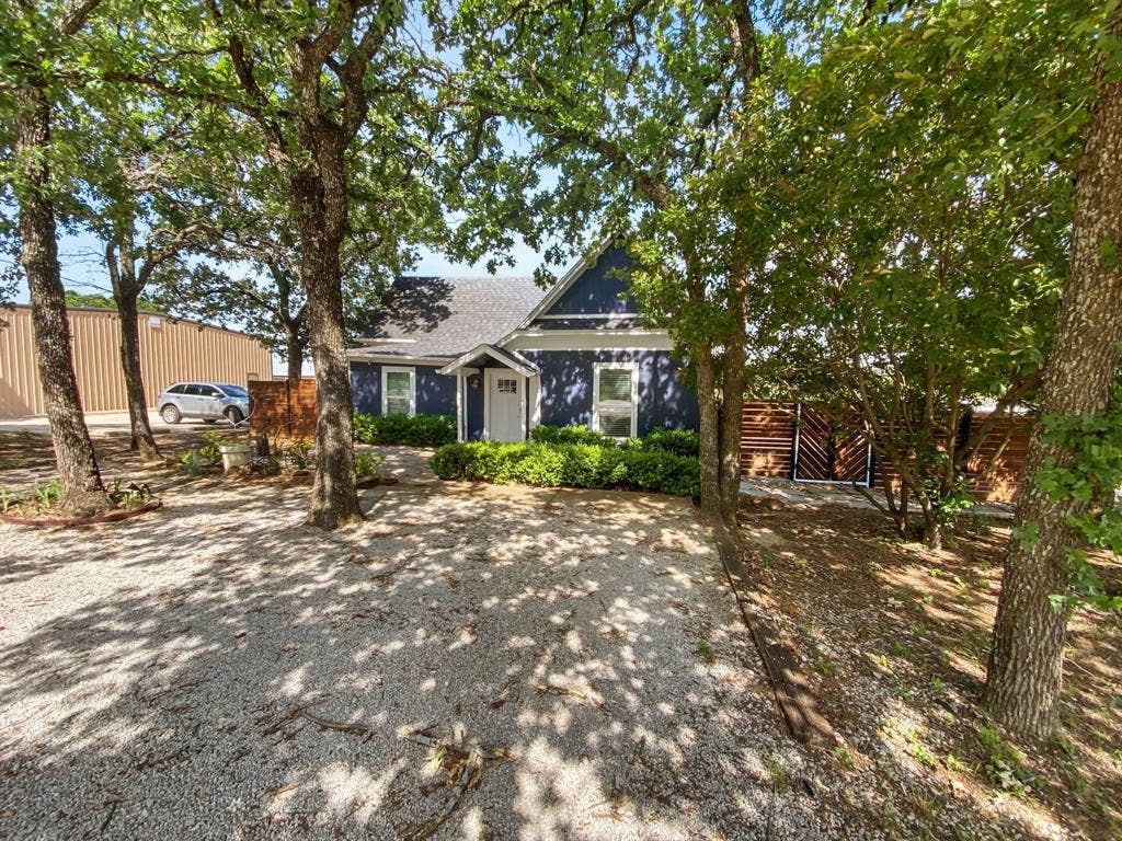 815 Stonecrest Road, Argyle, TX 76226 Deep blue exterior with white trim, covered front entry, gravel driveway, mature trees, and privacy fencing