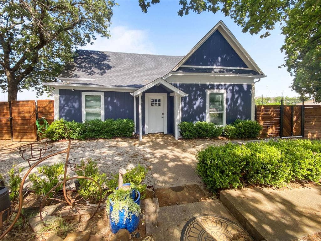 815 Stonecrest Road, Argyle, TX 76226 Blue exterior siding with white trim, a covered entry porch, dark gray shingle roof, and a wood-slat fence