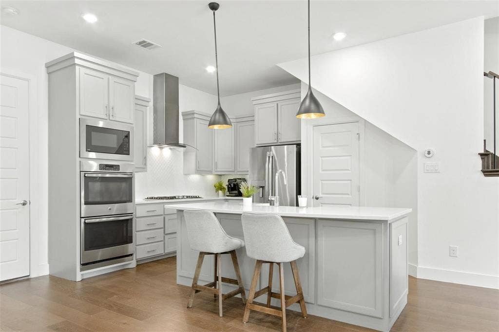 7867 Verona Place, Dallas, TX 75231 Open-concept kitchen featuring an island with seating, stainless steel appliances, light gray cabinetry, and wood-finish flooring