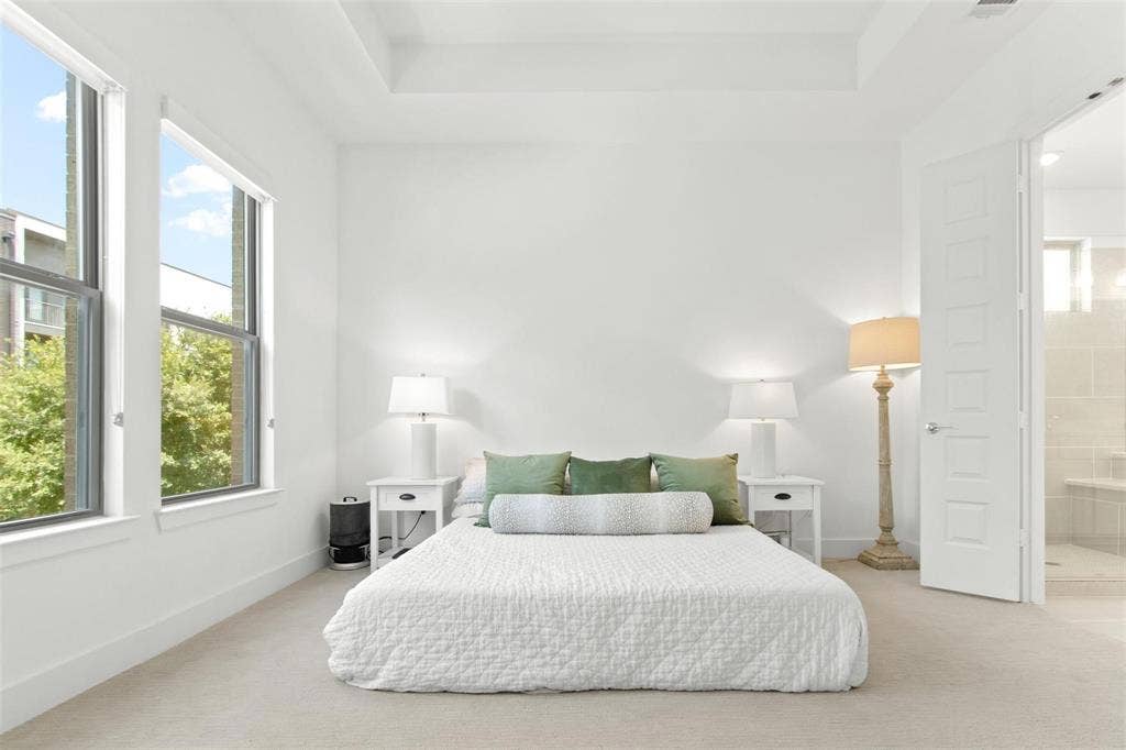 7867 Verona Place, Dallas, TX 75231 Carpeted room featuring a tray ceiling, two tall windows, and a panel door leading to a tiled bath area with a built-in bench