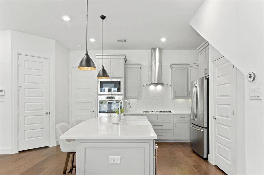 7867 Verona Place, Dallas, TX 75231 Contemporary kitchen featuring a large central island with seating, stainless steel appliances, light gray cabinetry, and a white subway tile backsplash