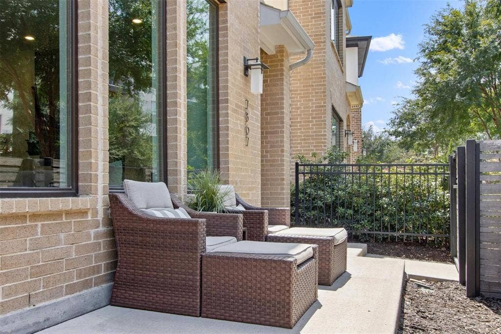 7867 Verona Place, Dallas, TX 75231 Brick exterior with multiple tall windows, featuring a concrete patio, black metal fencing, and a modern slatted gate
