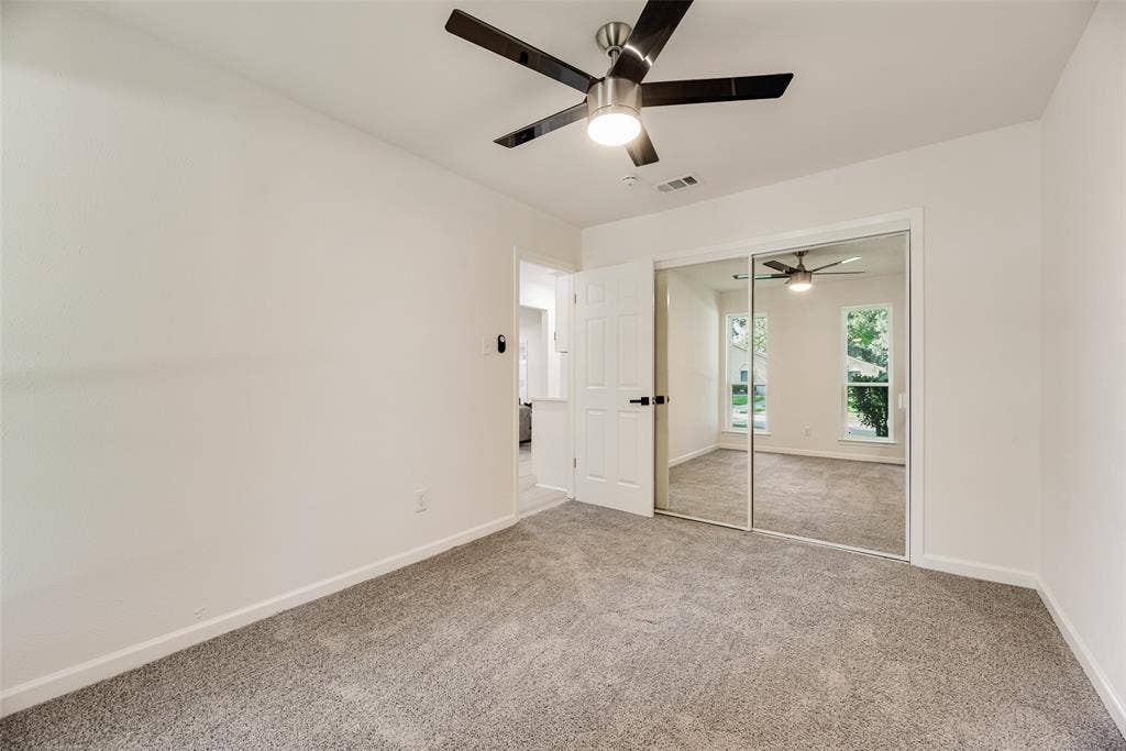 Carpeted room featuring a ceiling fan with integrated lighting, white walls, and a mirrored closet door