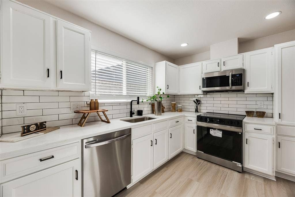 Bright, modern kitchen featuring white shaker-style cabinetry, white subway tile backsplash, and stainless steel appliances including a double wall oven, dishwasher, and microwave