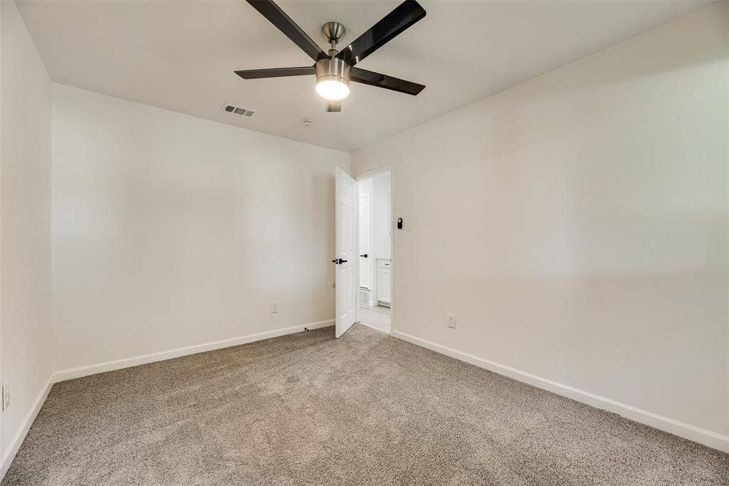 Spacious interior room featuring light gray carpet, white walls, and a ceiling fan with integrated lighting
