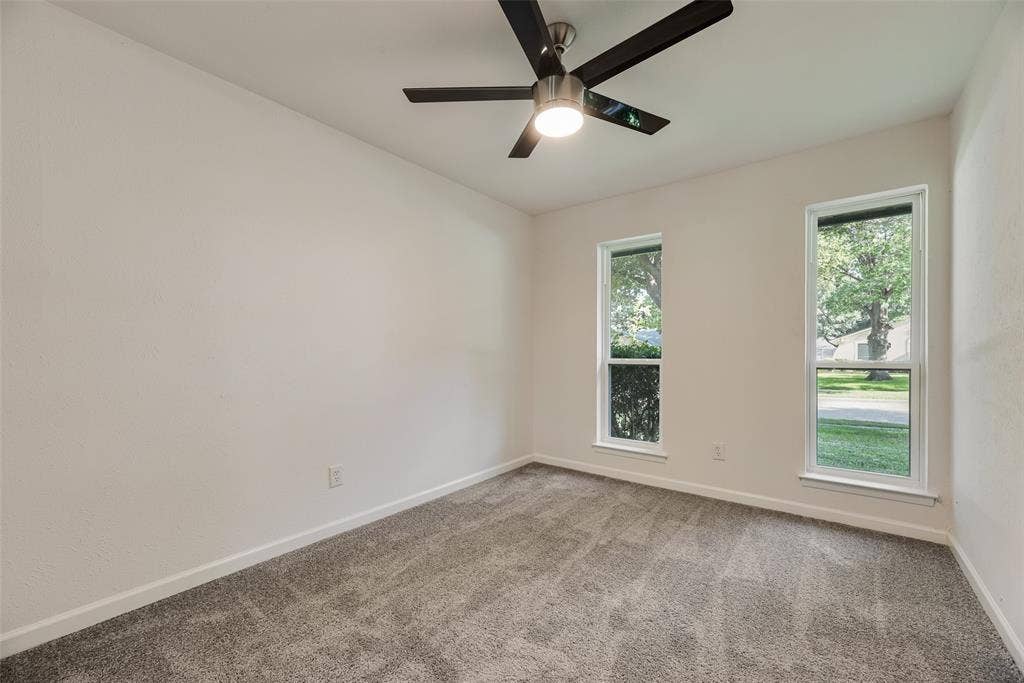 Neutral wall finishes featuring a ceiling fan with integrated lighting, two vertically oriented windows, and gray carpet flooring