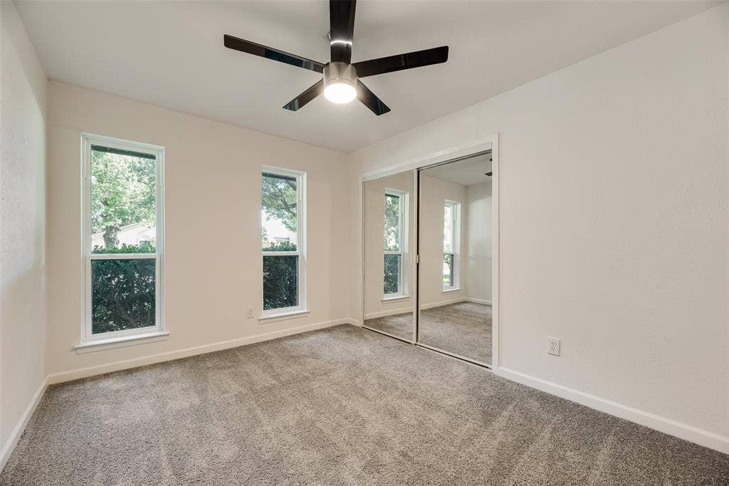 Carpeted room featuring two vertical windows with white trim, a contemporary ceiling fan, and mirrored closet doors