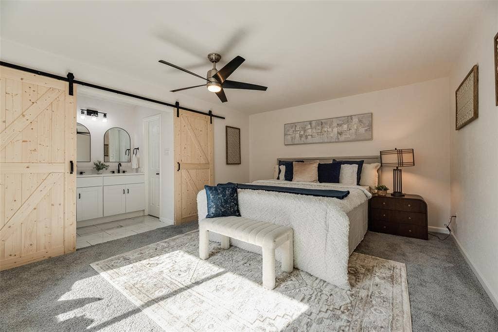 Carpeted room featuring a ceiling fan and barn door entry to a bathroom