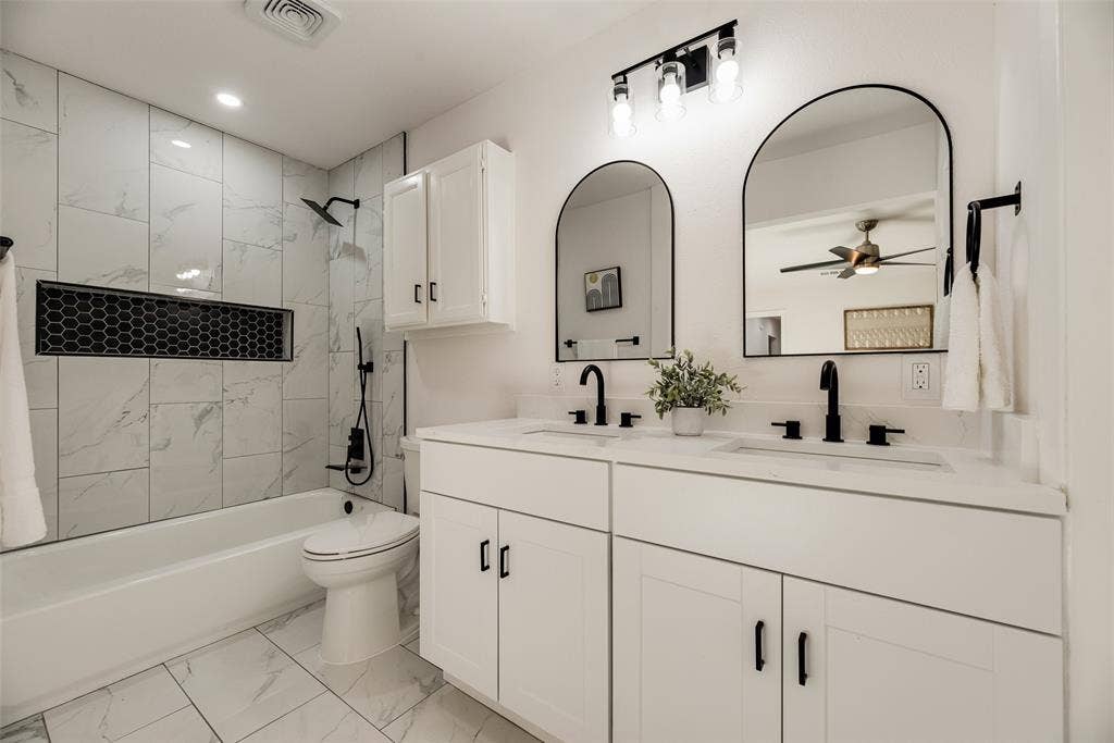 Contemporary bathroom featuring a double vanity with white cabinetry, matte black fixtures, and two arched mirrors