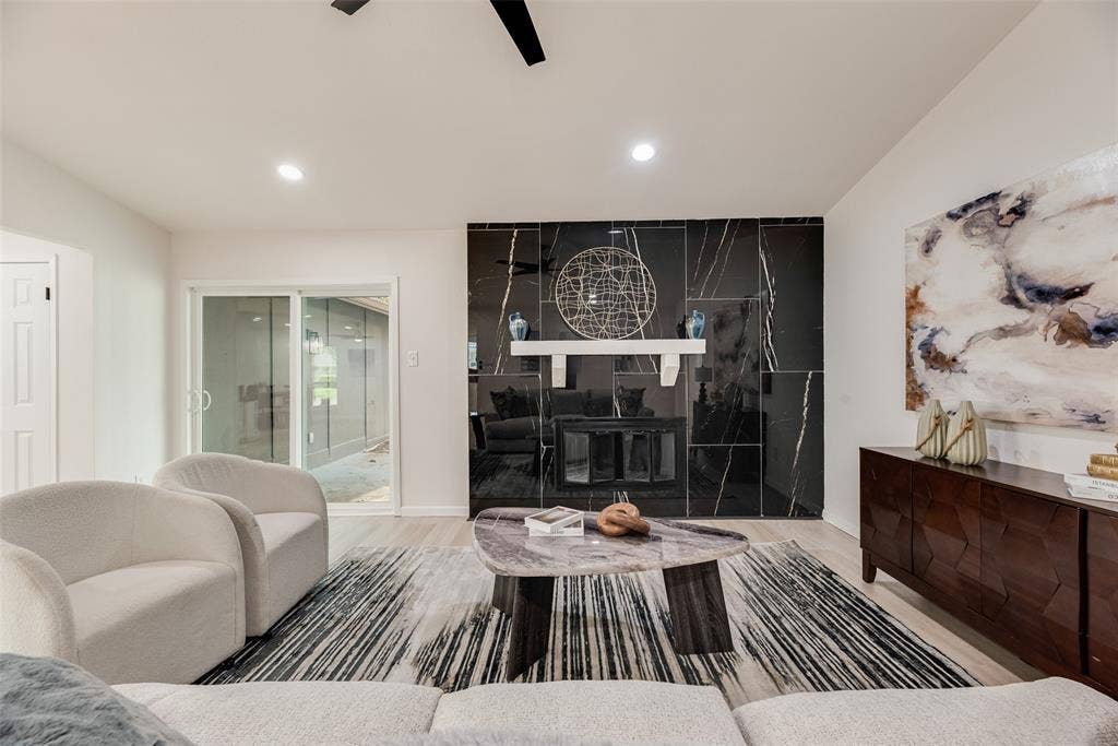 Living space featuring a striking black marble-look fireplace surround with a white mantel, ceiling-mounted lighting, and wood-finish flooring