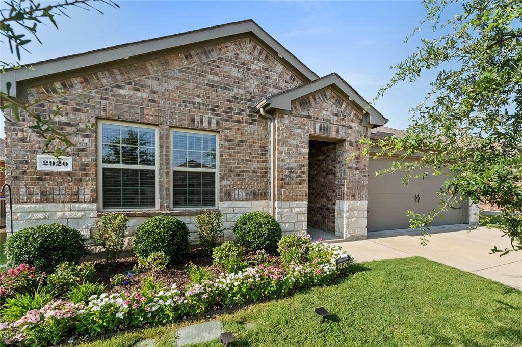 2920 Roper Street, Royse City, TX 75189 Brick and stone facade residence featuring a covered entry, an attached garage, and a landscaped front yard with decorative plantings