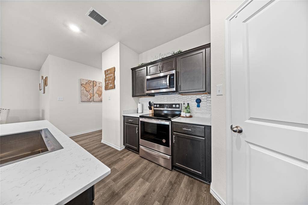 2920 Roper Street, Royse City, TX 75189 Kitchen featuring dark wood-finish cabinetry, stainless steel appliances including a microwave and range, light-toned countertops, and a white hexagonal tile backsplash