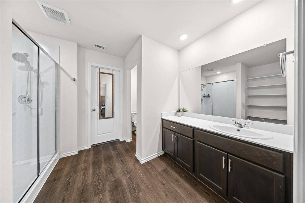 2920 Roper Street, Royse City, TX 75189 Spacious bathroom featuring a glass-enclosed shower, expansive vanity with a single basin sink, rich wood-finish cabinetry, and wood-finish flooring