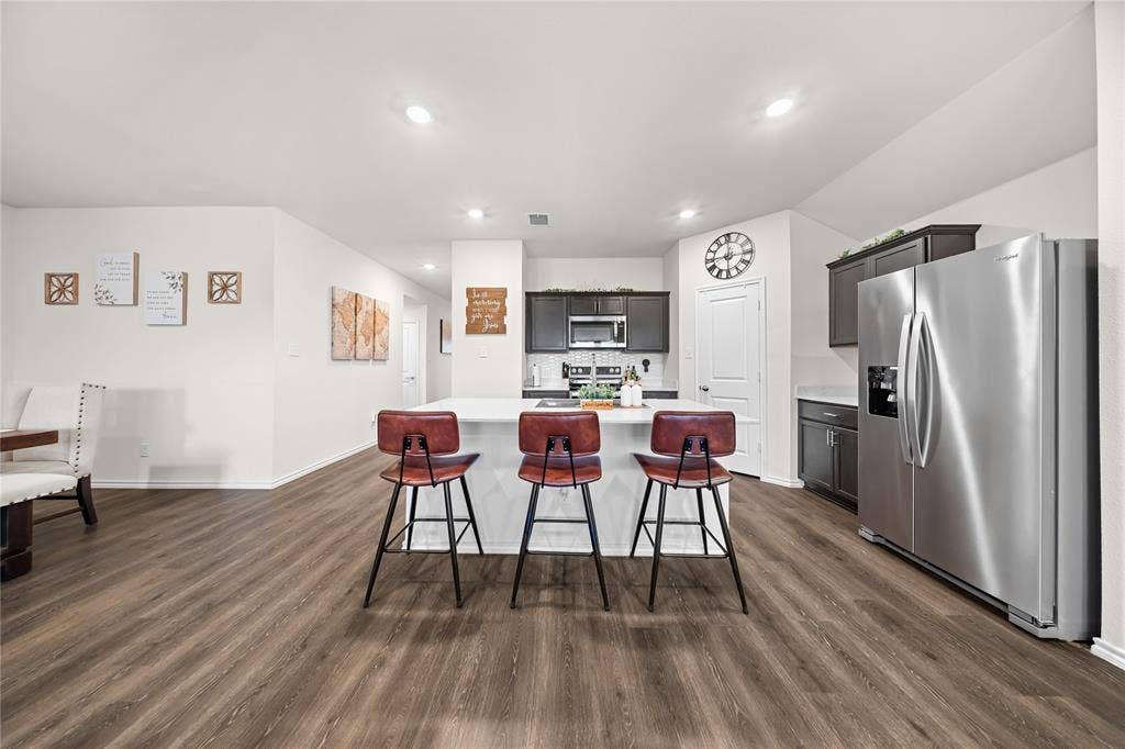 2920 Roper Street, Royse City, TX 75189 Open-concept kitchen featuring an island with seating, stainless steel appliances, dark wood cabinetry, light countertops, and wood-finish flooring