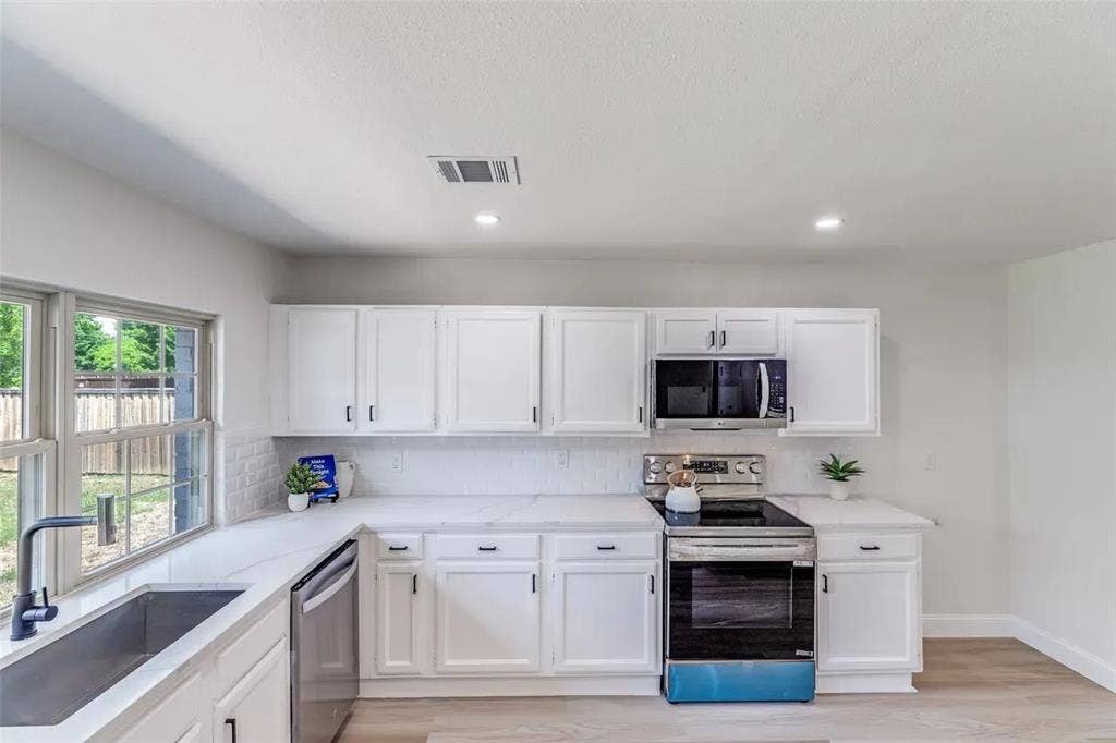 Modern kitchen featuring white cabinetry, light countertops, subway tile backsplash, and stainless steel appliances