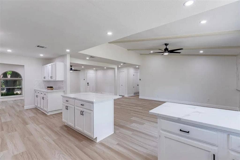 Bright and spacious kitchen featuring white cabinetry with hardware accents, a large center island with seating counter, stainless steel appliances, and wood-finish flooring throughout