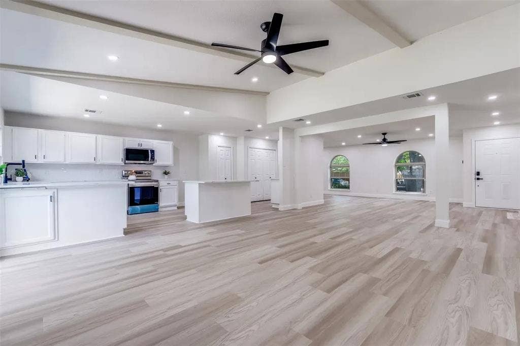 Expansive open-concept living area featuring light wood-finish flooring, recessed lighting, and exposed ceiling beams