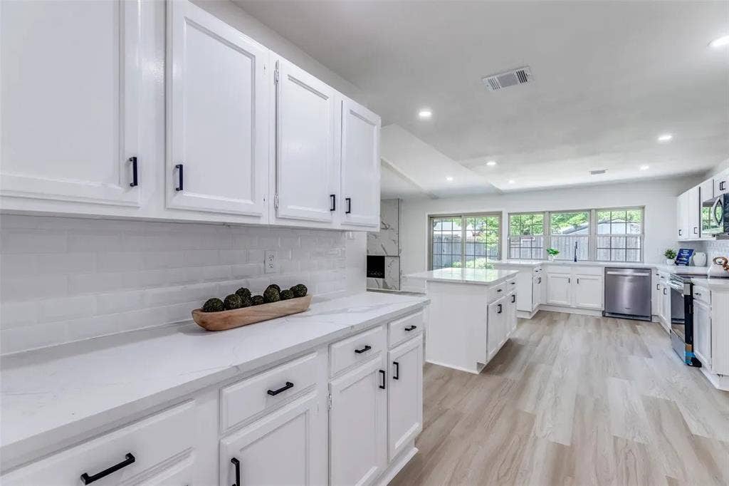 Bright, modern kitchen featuring crisp white cabinetry with black hardware, white subway tile backsplash, and stainless steel appliances