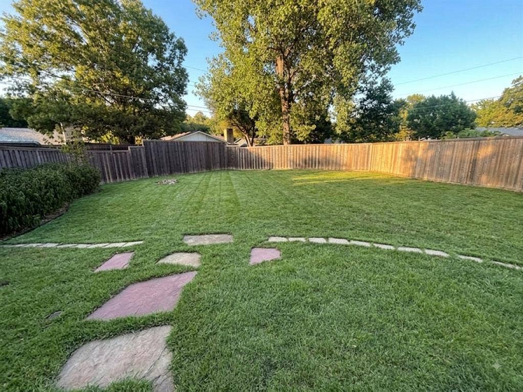 Expansive backyard with a manicured lawn, a full-height wood fence, and stone stepping-stones