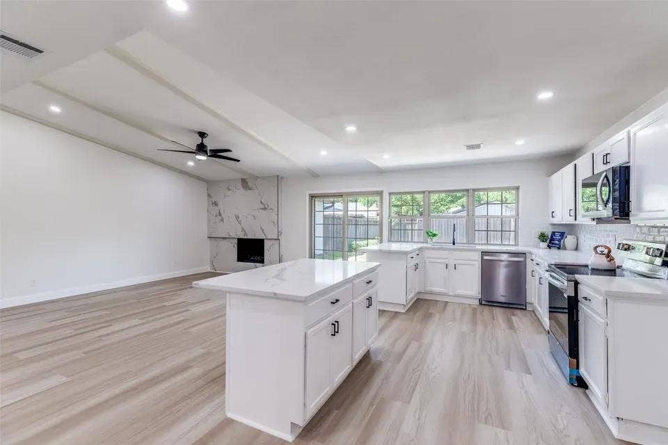 Bright, open-concept kitchen featuring white cabinetry with hardware accents, stainless steel appliances including a gas range and refrigerator, quartz countertops, and a substantial island with seating