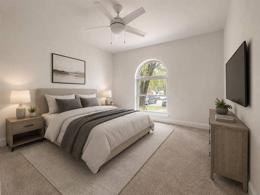 Arched window with exterior street perspective, ceiling fan with integrated lighting, carpeted flooring, and a wall-mounted flat screen television