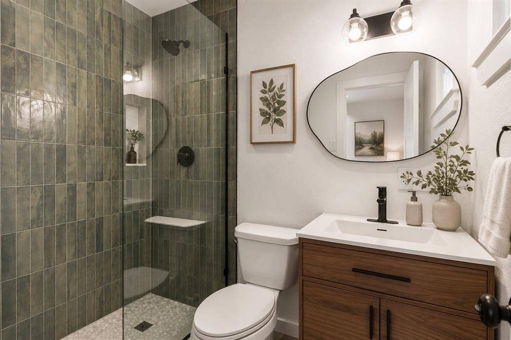2251 Hartline Drive, Dallas, TX 75228 A frameless glass shower showcases elegant artisan-inspired green title extending floor to ceiling, creating a calming, spa-like retreat. The warm walnut vanity adds rich natural character and contrasts beautifully with the sleek white quartz countertop and contemporary vessel-style sink. Matte black fixtures, an organically shaped designer mirror