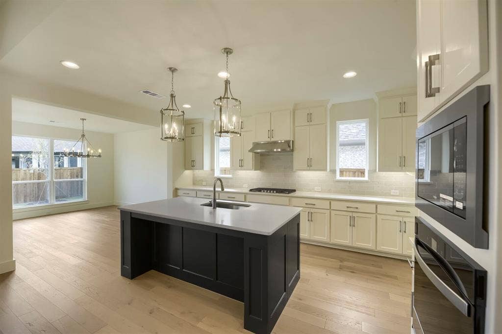 690 Red Cedar Road, Haslet, TX 76052 Open-concept kitchen featuring a dark-toned island with a light countertop, white cabinetry, integrated stainless steel appliances, and wood-finish flooring