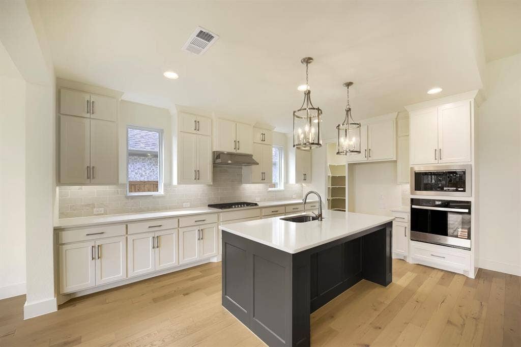 690 Red Cedar Road, Haslet, TX 76052 Kitchen featuring a large central island with undermount sink, pendant lighting, built-in stainless steel appliances, light-toned wood-finish flooring, and white cabinetry