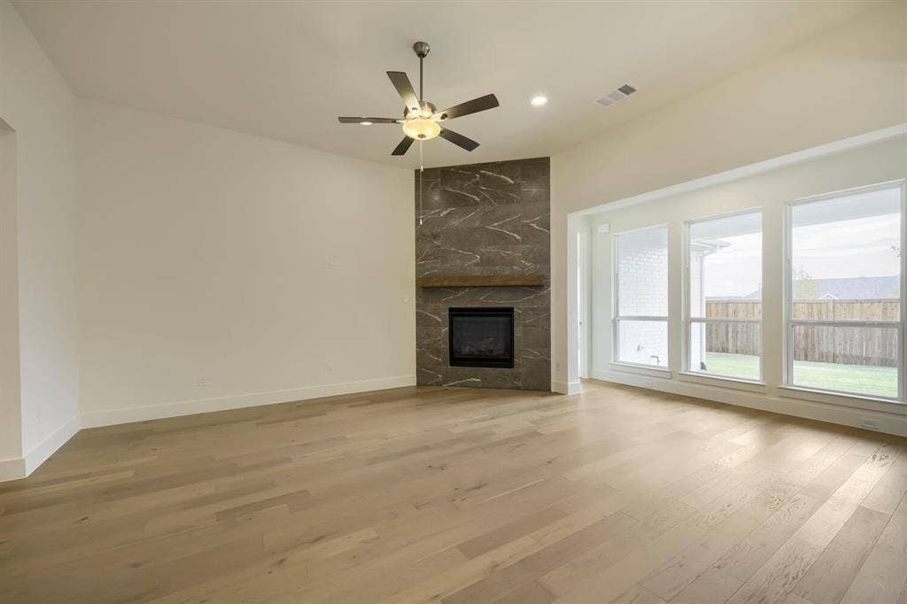 690 Red Cedar Road, Haslet, TX 76052 Vaulted ceiling featuring a ceiling fan, a fireplace with a stone-finish surround and wood-finish mantel, wood-finish flooring, and multiple windows