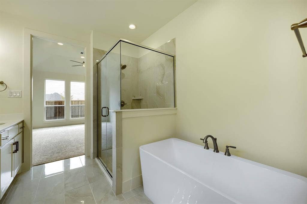 690 Red Cedar Road, Haslet, TX 76052 Tile flooring, freestanding bathtub with bronze-finish fixtures, glass-enclosed shower with tile surround, vanity with white cabinetry and light-colored countertop
