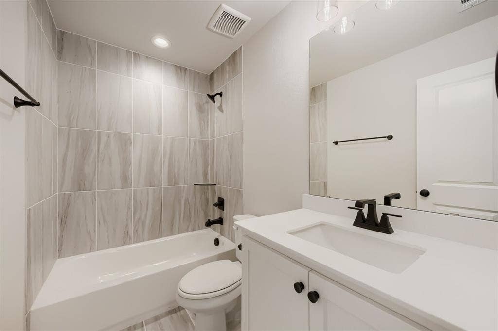 1281 White Pine Drive, Haslet, TX 76052 Bathtub with light-toned tiled surround, white vanity with integrated sink, white countertop, and dark-toned fixtures