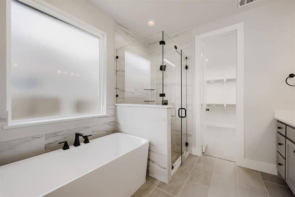 1281 White Pine Drive, Haslet, TX 76052 Freestanding soaking tub with matte black fixtures, framed glass shower, marble-finish wall tile, and light-toned floor tile