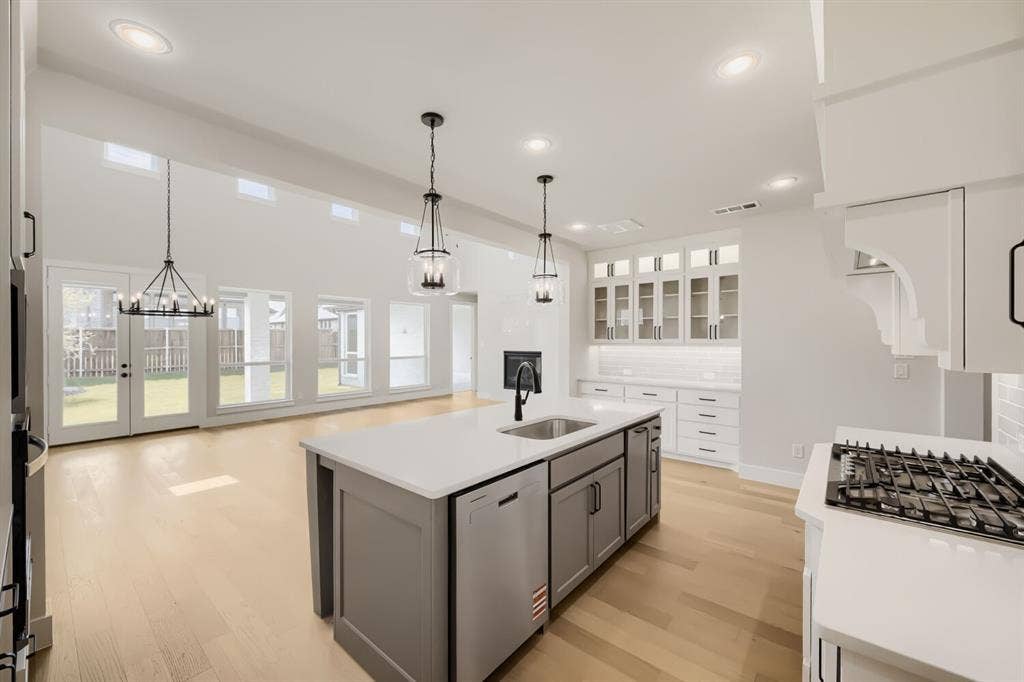 1281 White Pine Drive, Haslet, TX 76052 Open-concept kitchen and living area featuring a large center island with integrated sink, white subway tile backsplash, light wood-finish flooring, and a bank of glass-paneled cabinetry