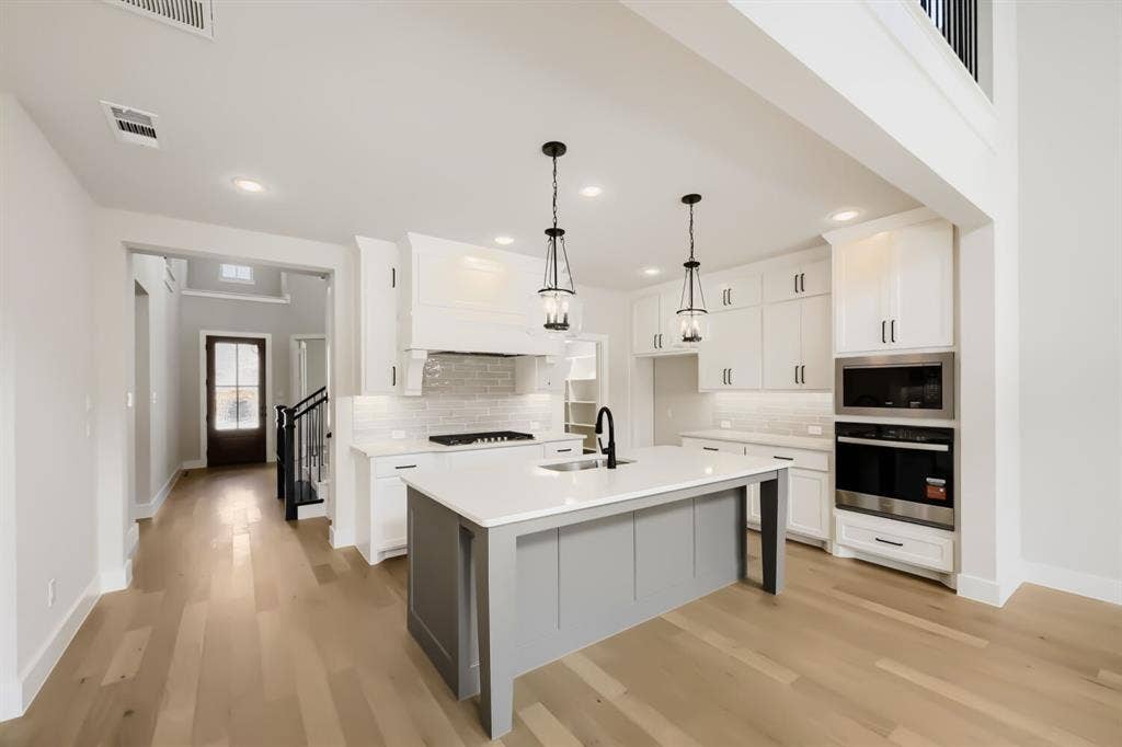 1281 White Pine Drive, Haslet, TX 76052 Open-concept kitchen featuring a large central island, white cabinetry, integrated stainless steel appliances, and wood-finish flooring