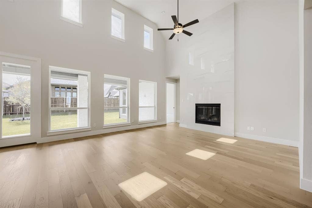1281 White Pine Drive, Haslet, TX 76052 Vaulted ceilings with a ceiling fan, a fireplace with a light-colored surround, wood-finish flooring, and multiple large windows