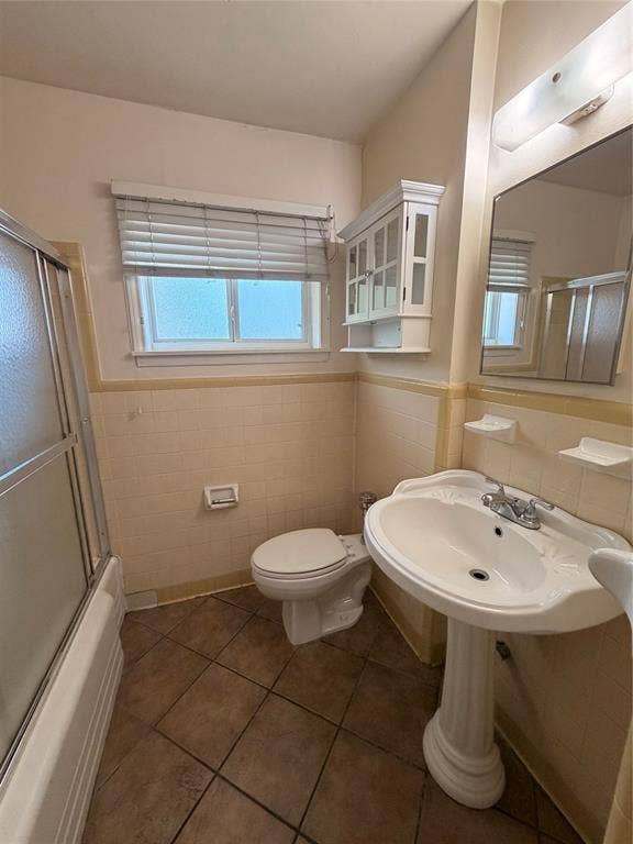5106 Reiger Avenue, Dallas, TX 75214 Bathroom featuring a ceramic pedestal sink, tiled wall wainscoting, glass-enclosed shower, wall-mounted white cabinetry, and ceramic tile flooring