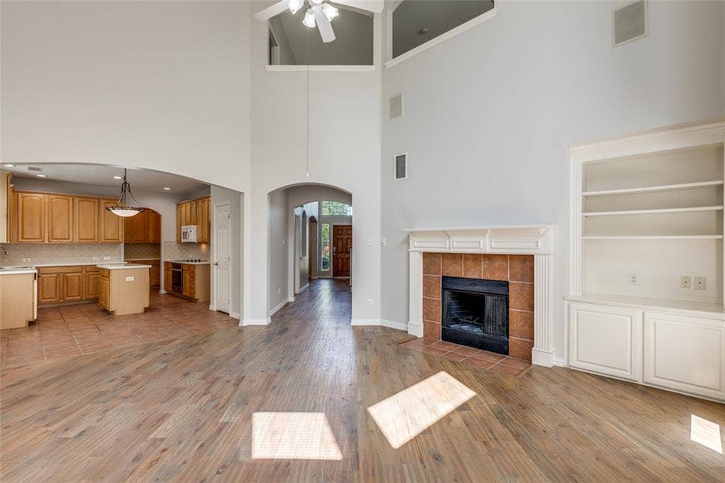 3401 Maddock Drive, McKinney, TX 75070 Two-story living area with wood-finish flooring, a tile-surround fireplace with mantel, and built-in shelving