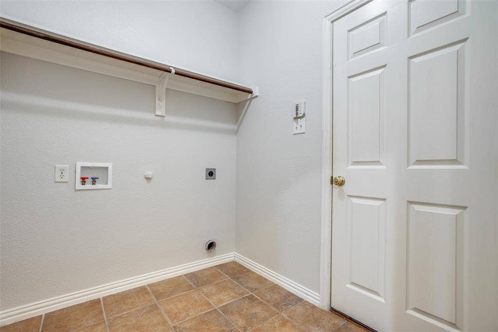 3401 Maddock Drive, McKinney, TX 75070 Utility room featuring ceramic tile flooring, wall-mounted shelving with bracket support, electrical outlets, and a six-panel white entry door with brass hardware