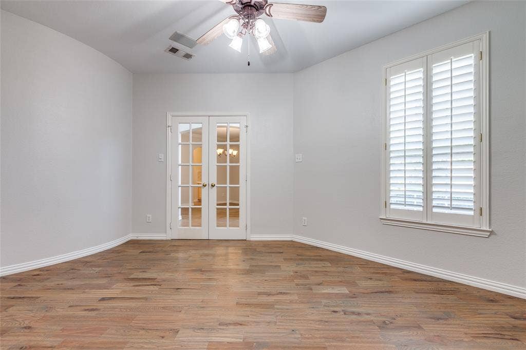3401 Maddock Drive, McKinney, TX 75070 Spacious room showcasing warm wood-finish flooring, white painted walls, and abundant natural light from dual shuttered windows