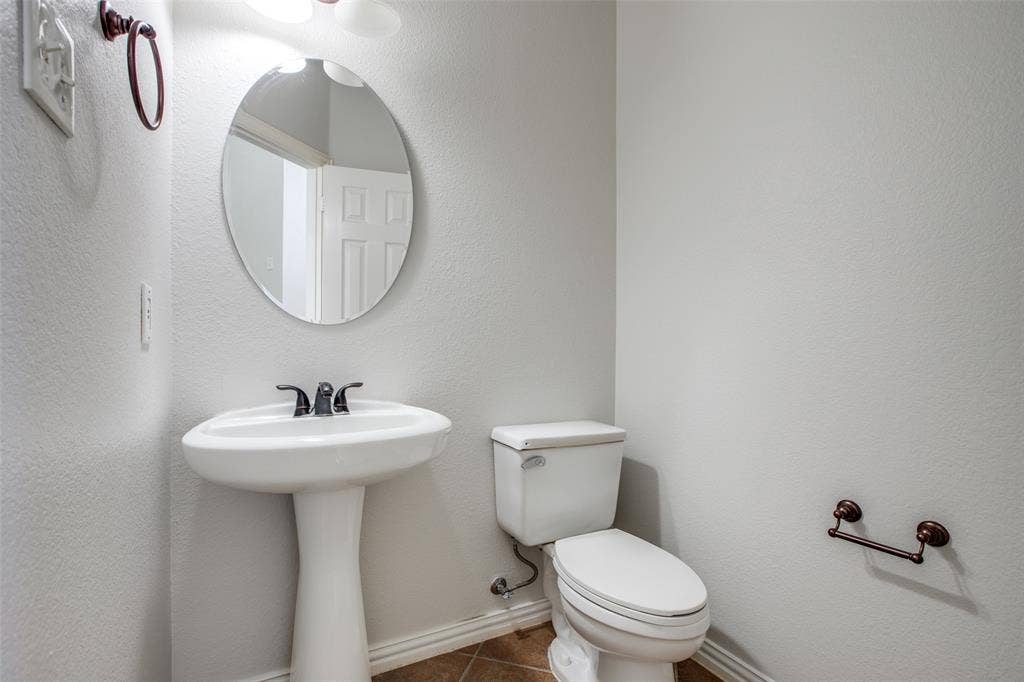3401 Maddock Drive, McKinney, TX 75070 Powder room featuring a pedestal sink with oil-rubbed bronze faucet and hardware, a round mirror with metal frame, a toilet with chrome tank lever, and wood-finish flooring