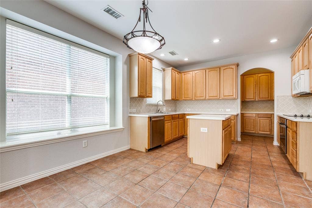 3401 Maddock Drive, McKinney, TX 75070 Spacious kitchen featuring wood-finish cabinetry, tile flooring, a central island with prep space, large windows with natural light, and a doorway opening to additional living areas