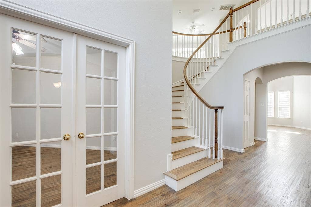3401 Maddock Drive, McKinney, TX 75070 Elegant foyer showcasing a curved staircase with wood treads and brass railings, gleaming wood-finish flooring, and French doors with multiple glass panes leading to adjacent spaces