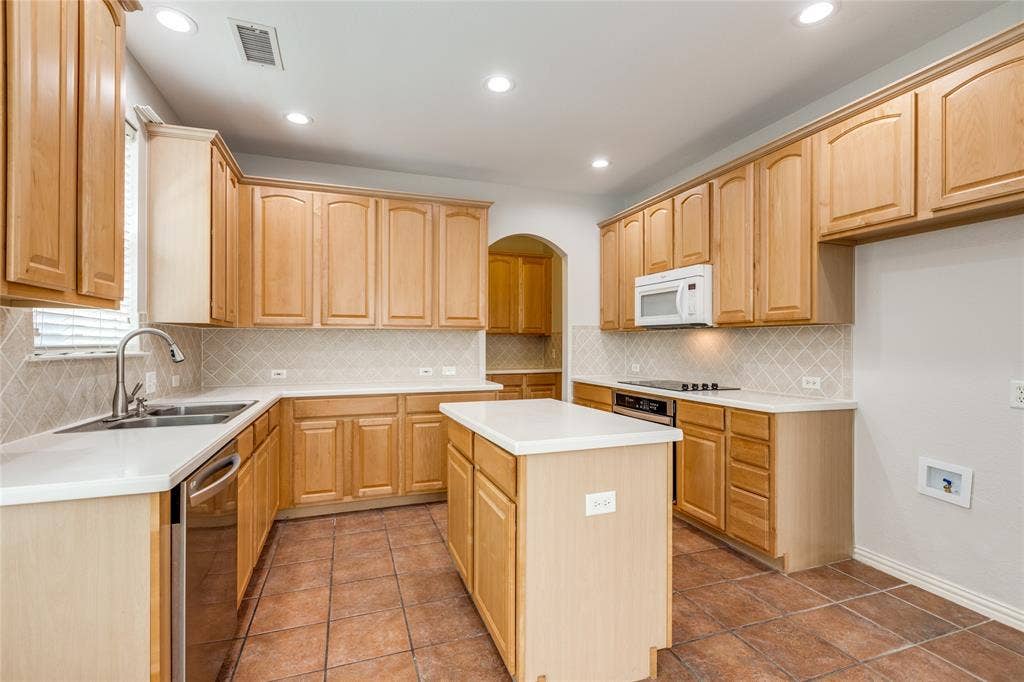 3401 Maddock Drive, McKinney, TX 75070 Spacious kitchen featuring warm wood cabinetry throughout, white countertops, tile flooring, a center island with additional counter space, stainless steel appliances, recessed lighting, and a convenient pass-through opening to an adjacent room